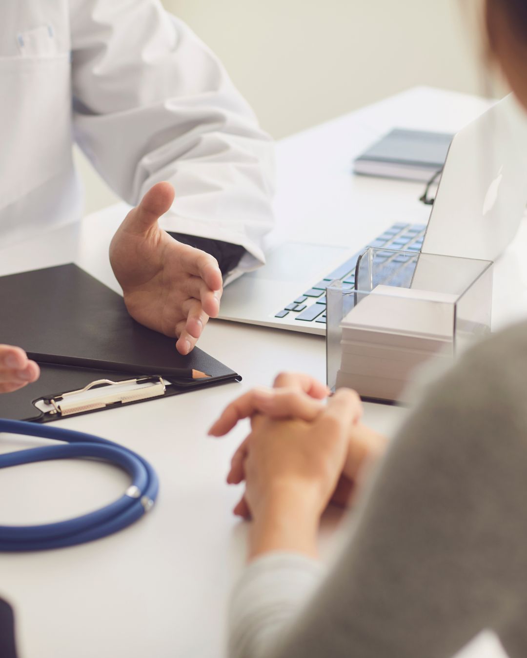 Doctor gesturing during a consultation at a desk with a patient and medical supplies
