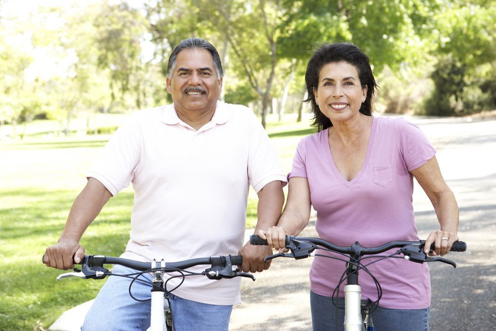 Two people smiling while standing with bicycles in a sunny park