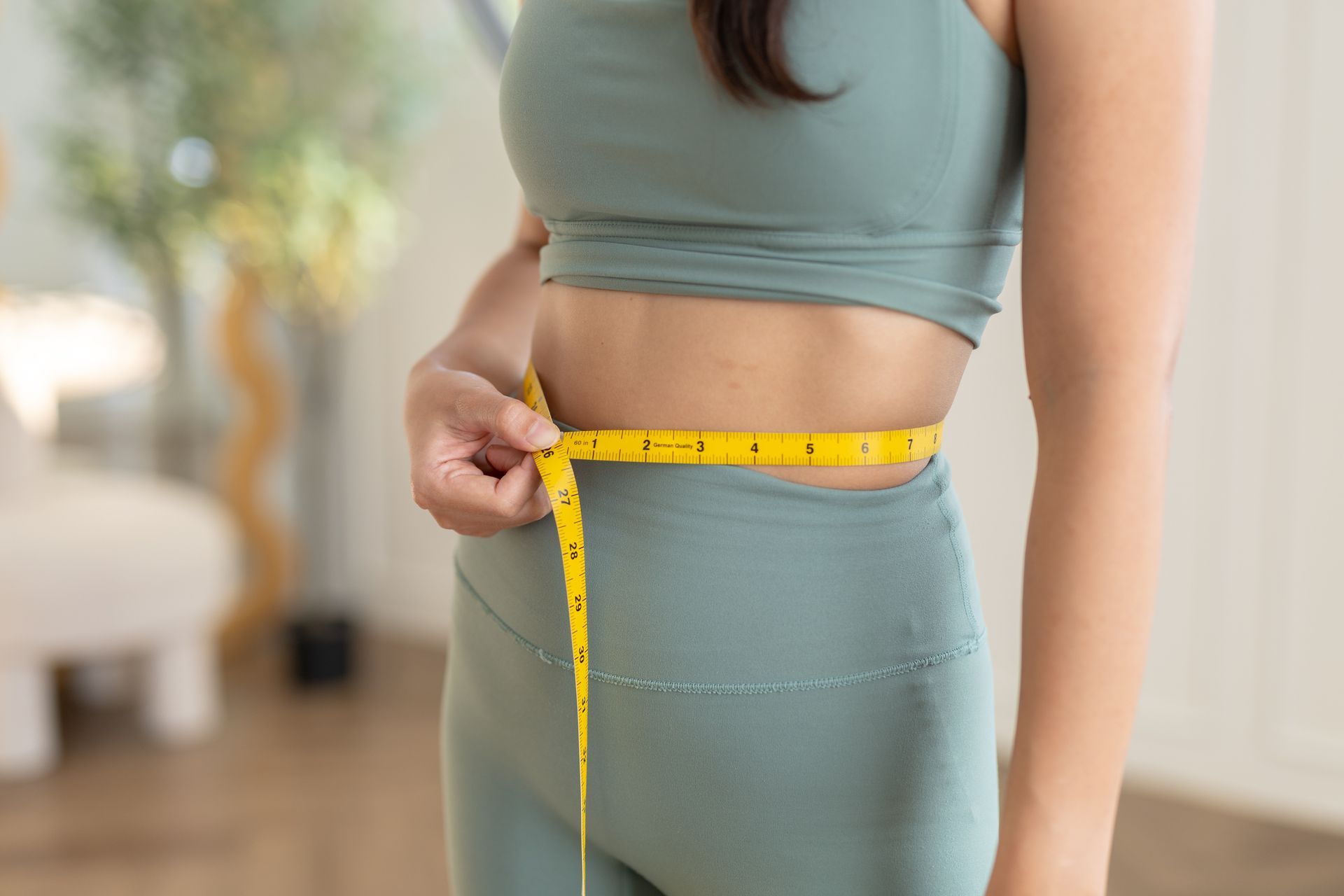 Person measuring waist with a yellow tape measure while wearing teal activewear.