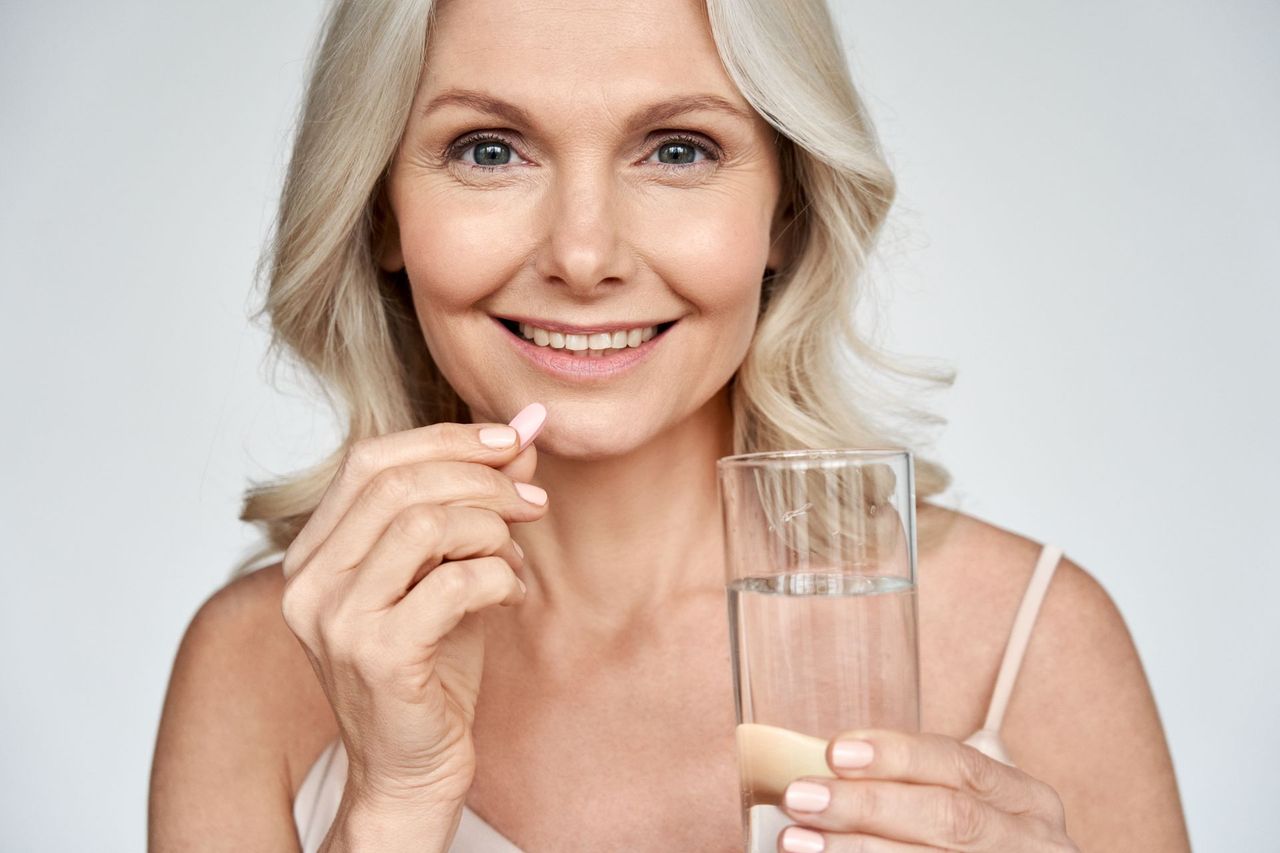 Smiling woman holding a glass of water and a pill against a white background