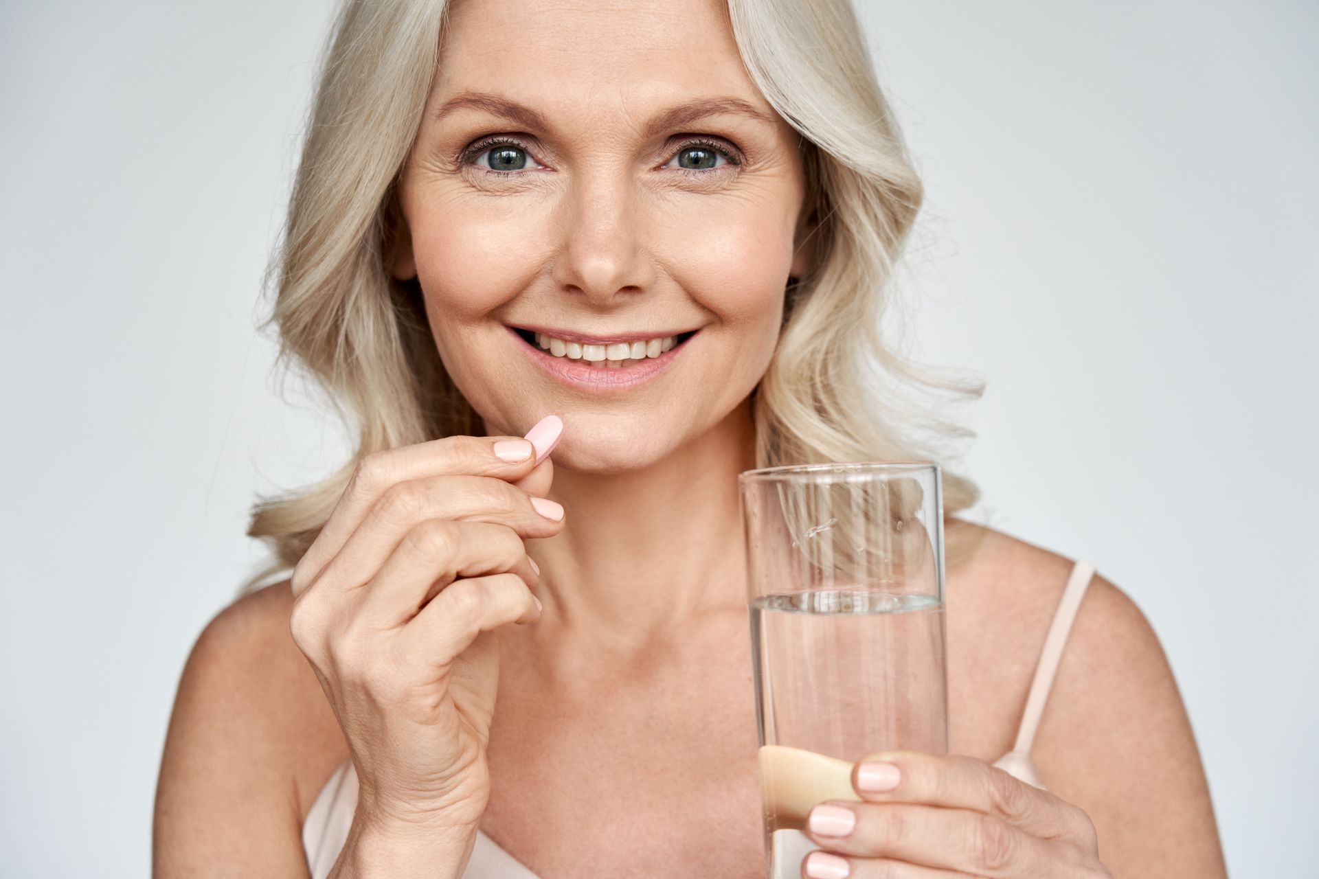 Smiling woman holding a glass of water and a pill against a white background