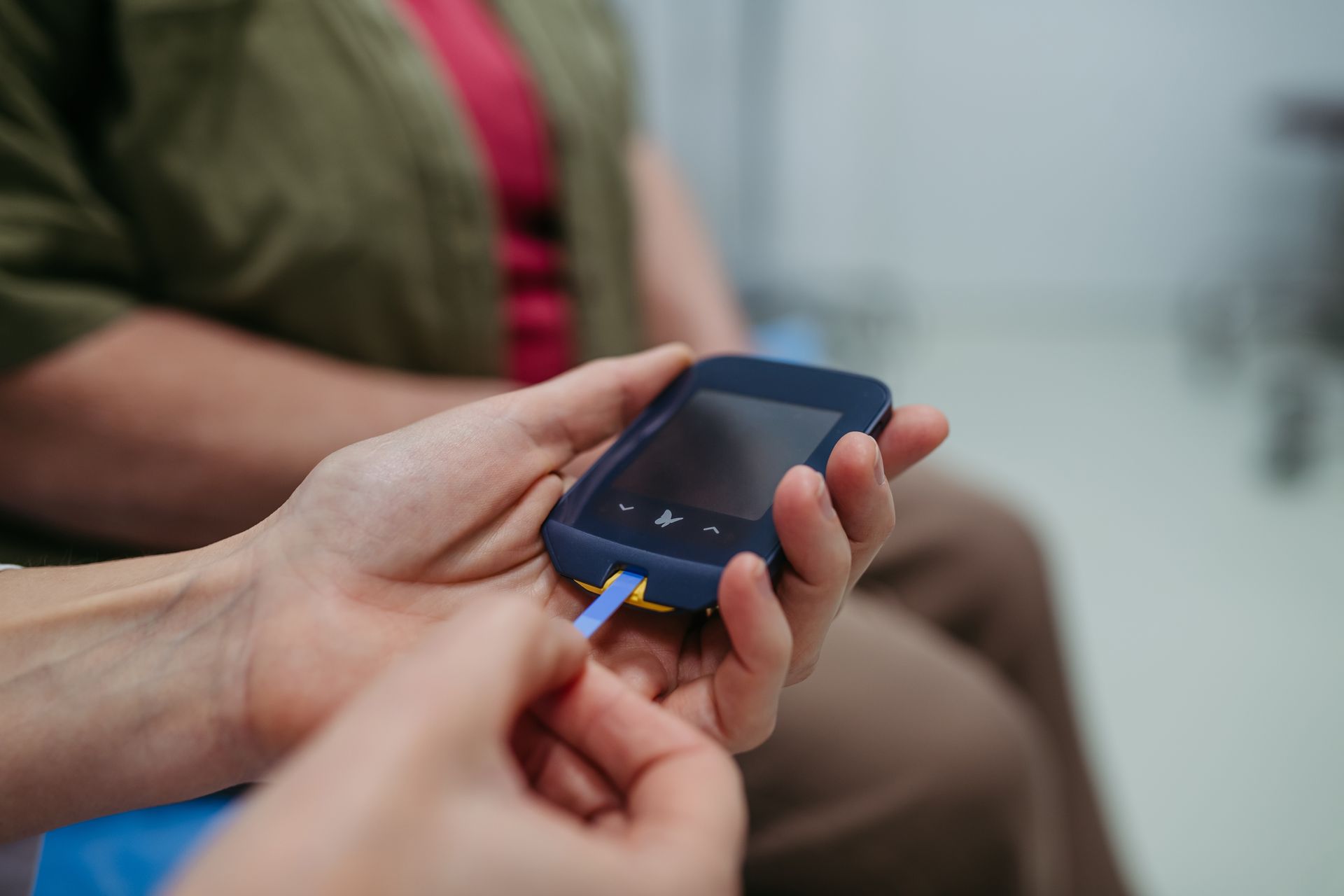 Hands holding a smartphone with a yellow cable connected, in a blurred indoor setting